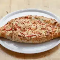 Khachapuri Géorgien : Pain Fromage Fondant Authentique Khachapuri géorgien allongé, garni de fromage fondu et de tranches de tomate, servi sur une assiette blanche ovale.
