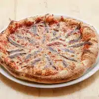 Pizza Anchois Artisanale : Goût Traditionnel & Croûte Dorée Pizza napolitaine cuite au four, garnie de sauce tomate, fromage et disposée artistiquement de filets d'anchois.