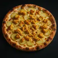 Pizza Poulet et Pommes de Terre Originale et Gourmande Pizza garnie de morceaux de poulet doré et de fines tranches de pommes de terre sur une base de fromage crémeux, vue de dessus sur fond noir.