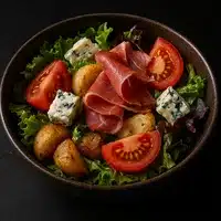 Salade Rustique Jambon Cru, Pommes de Terre et Fromage Bleu Salade gourmande avec pommes de terre rôties, tranches de tomates, dés de fromage bleu persillé, et fines tranches de jambon cru sur un lit de laitue verte.