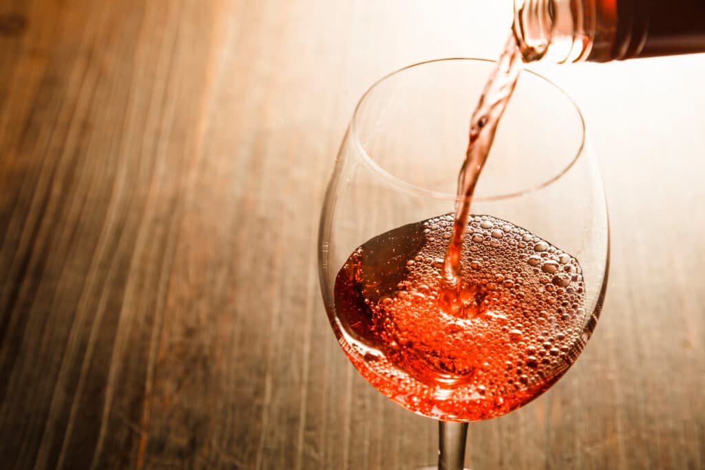Vin Rosé Pétillant Versé dans un Verre sur Bois Verseur de vin rosé pétillant dans un verre, créant une mousse de bulles sur fond de bois sombre.