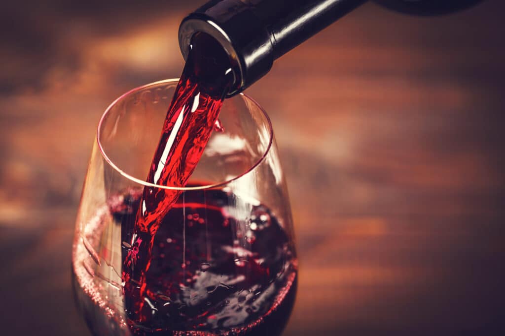 Vin Rouge Versé dans un Verre - Dégustation Gros plan d'un vin rouge riche et foncé versé d'une bouteille dans un verre à vin, créant des remous intenses.